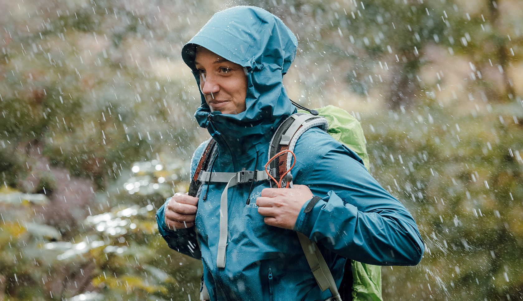 vrouw loopt door de regen met een hardshell en tas op de rug