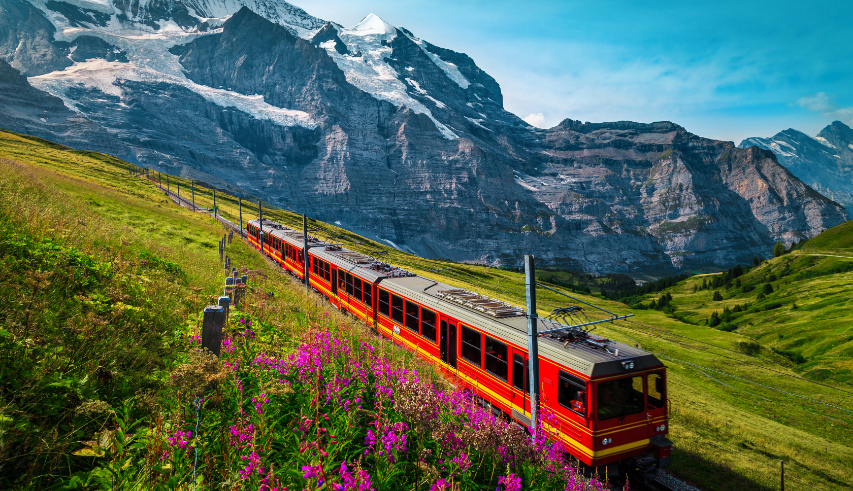 Een rode trein rijdt door een alpenweide met bergtoppen op de achtergrond