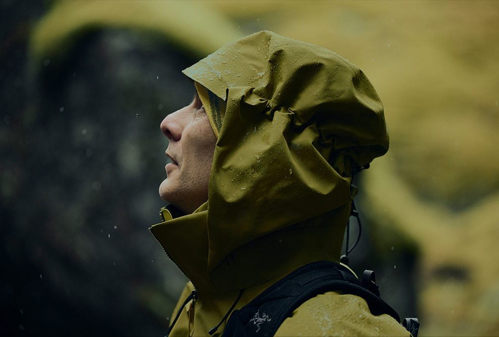 man in groene jas met capuchon op kijkt omhoog