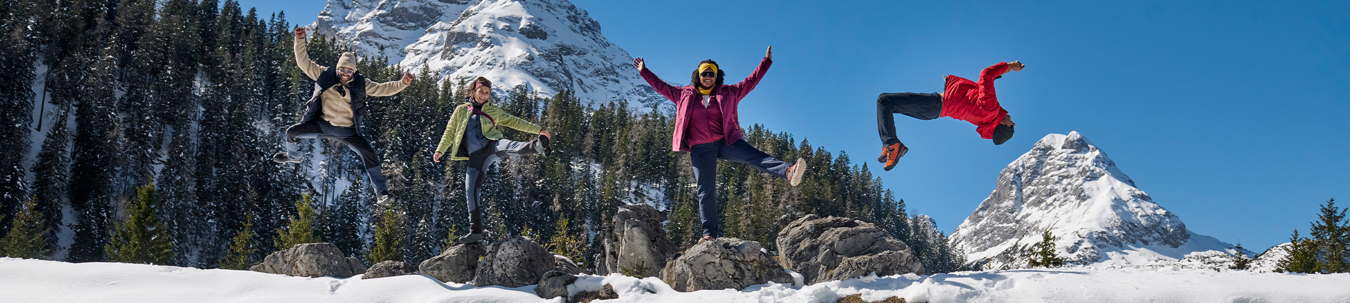 vier mensen springen in de lucht op een besneeuwde berg
