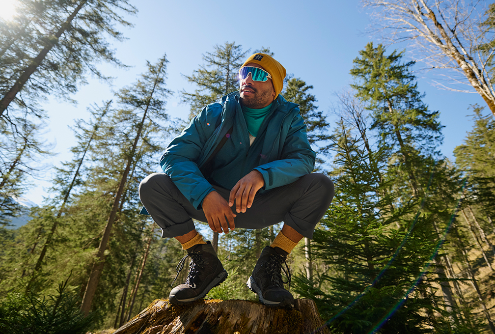 man gehurkt op boomstronk in bos