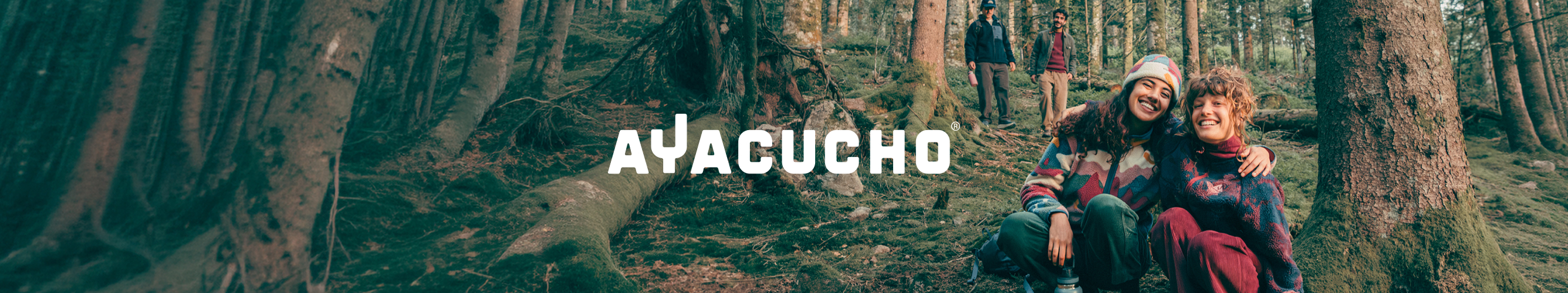 Vier wandelaars in een bos gekleed in Ayacucho-outdoorkleding, met het Ayacucho-logo centraal in beeld.Vier wandelaars in een bos gekleed in Ayacucho-outdoorkleding, met het Ayacucho-logo centraal in beeld.