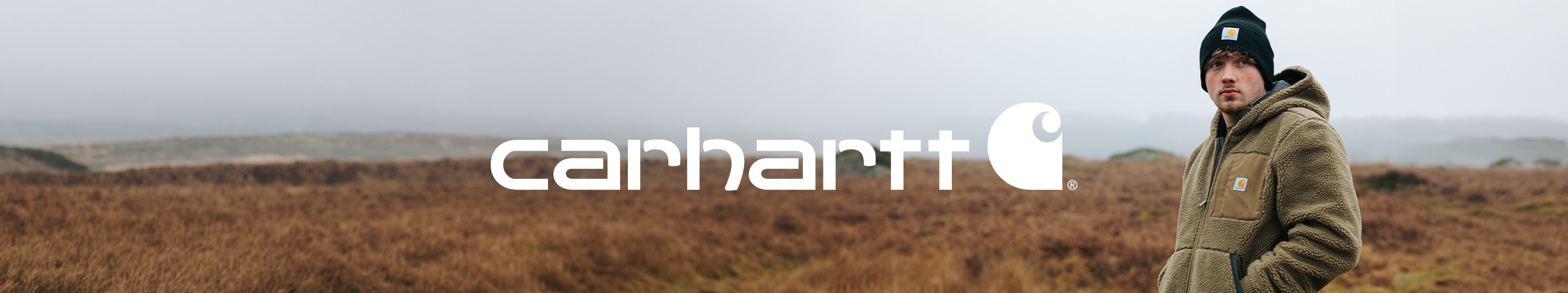 Man in een groene Carhartt fleecejas en muts in een open natuurlandschap