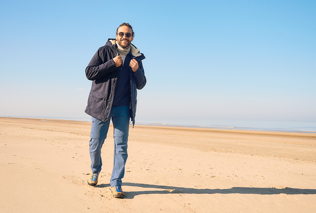 Man in Maier Sports-outdoorkleding tijdens een wandeling op het strand